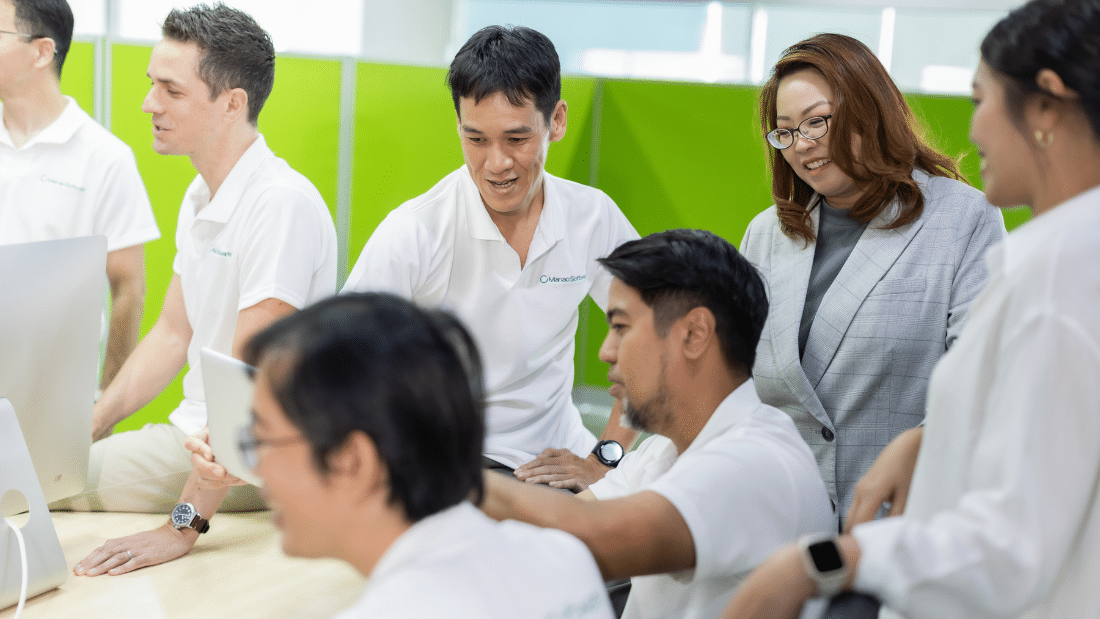 Several individuals in white shirts gathered around a computer, engaged in discussion and teamwork.